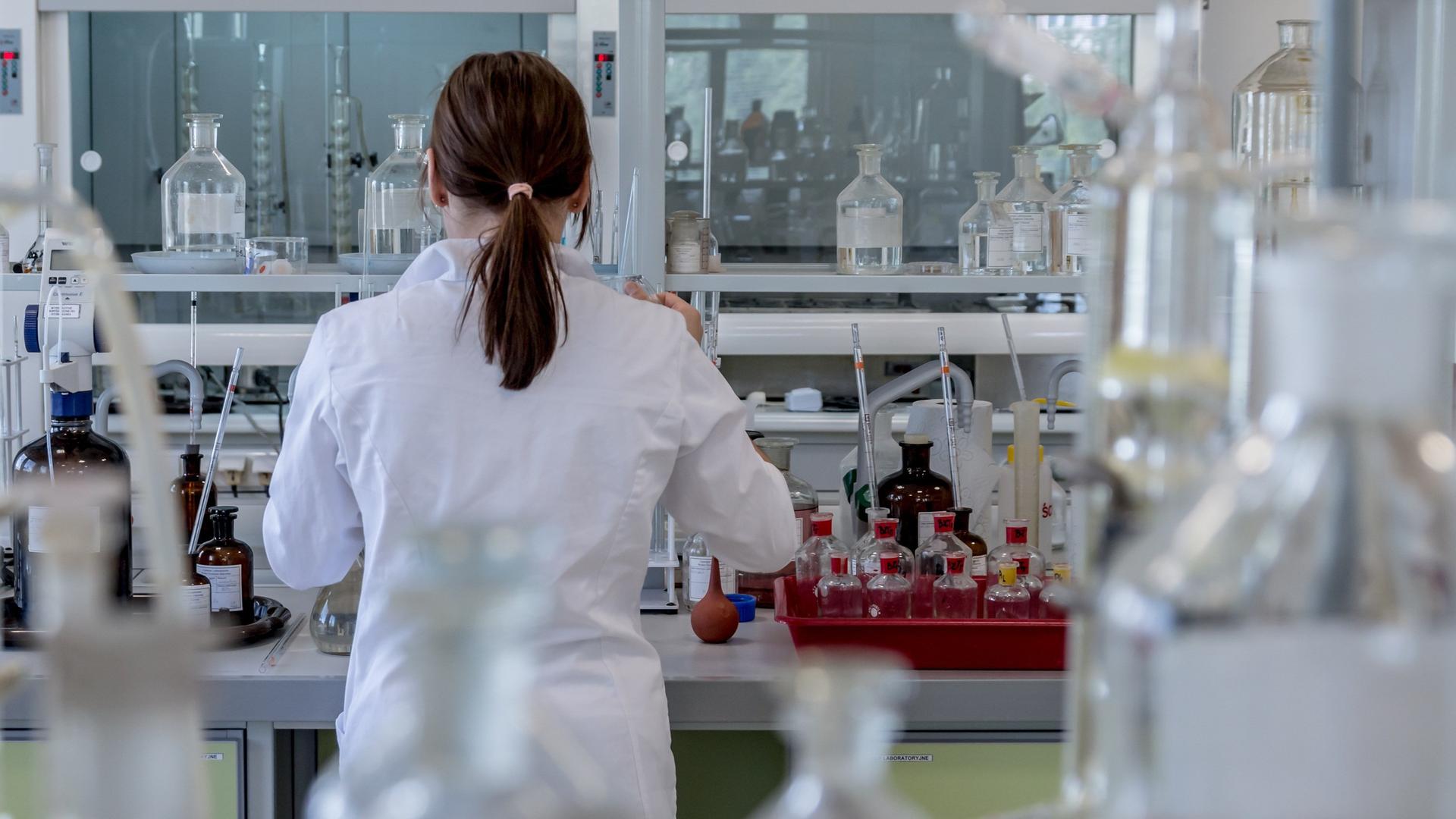 Mehr Frauen starten ins Studium als Männer – doch auf dem Weg zur Professur verschwinden viele aus der Wissenschaft. (Bild zeigt Forscherin von hinten im einem Labor)