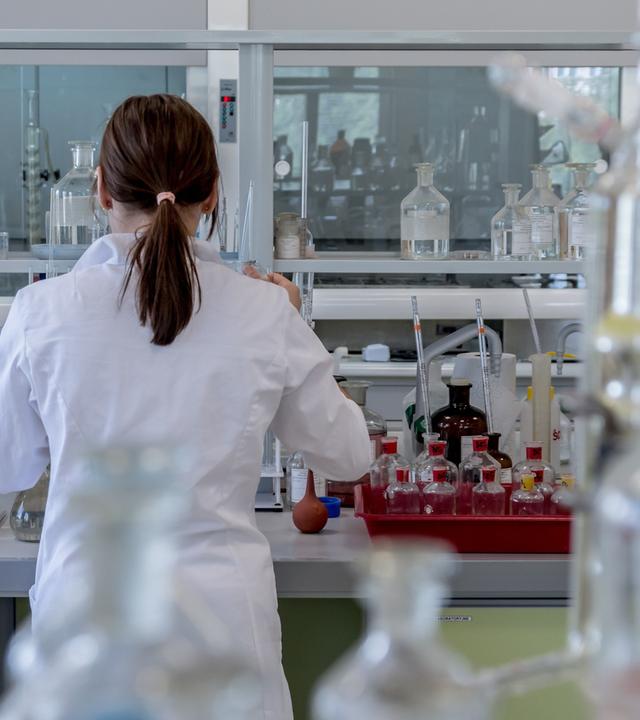 Mehr Frauen starten ins Studium als Männer – doch auf dem Weg zur Professur verschwinden viele aus der Wissenschaft. (Bild zeigt Forscherin von hinten im einem Labor)