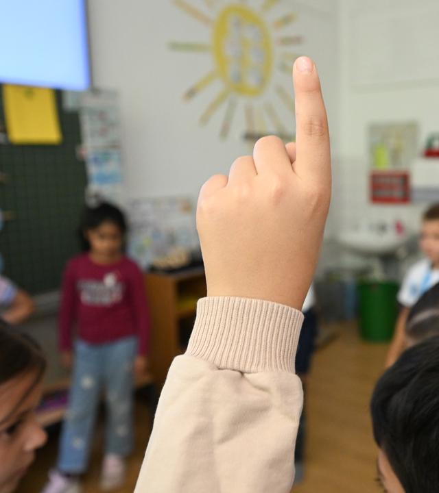 Lehrermangelctrifft Schüler an Schulen in benachteiligter Lage besonders. Was muss sich ändern? (Bild zeigt Unterricht im Klassenzimmer, im Vordergrund ein nach oben gestreckter Arm)