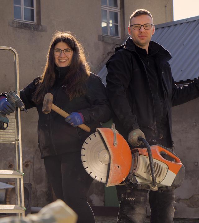 Julia und Max stehen mit Werkzeug vor ihrem Hof.