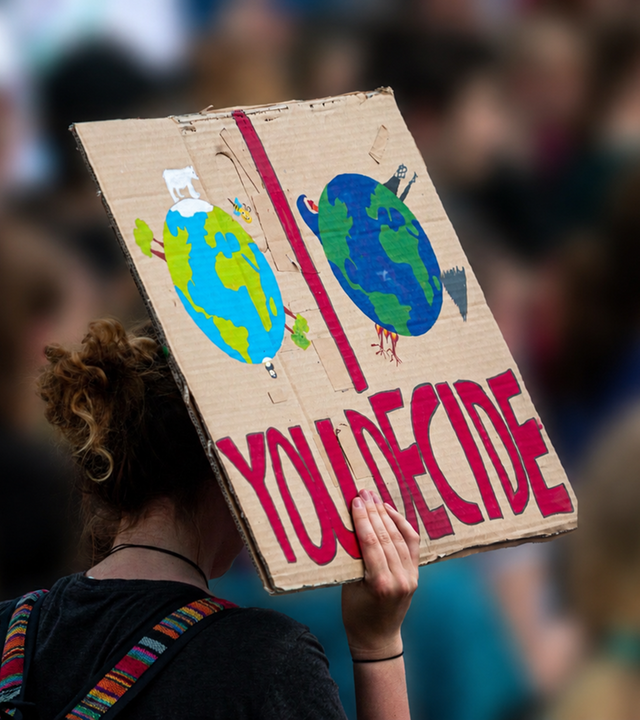 Auf der Bonner UN-Klimazwischenkonferenz zur COP31 erhöhen junge Menschen den Druck auf Deligierte und Konferenzteilnehmer. (Auf dem Bild ist eine Frau von hinten zu sehen, die ein Schild mit Aufschrift hochhält)