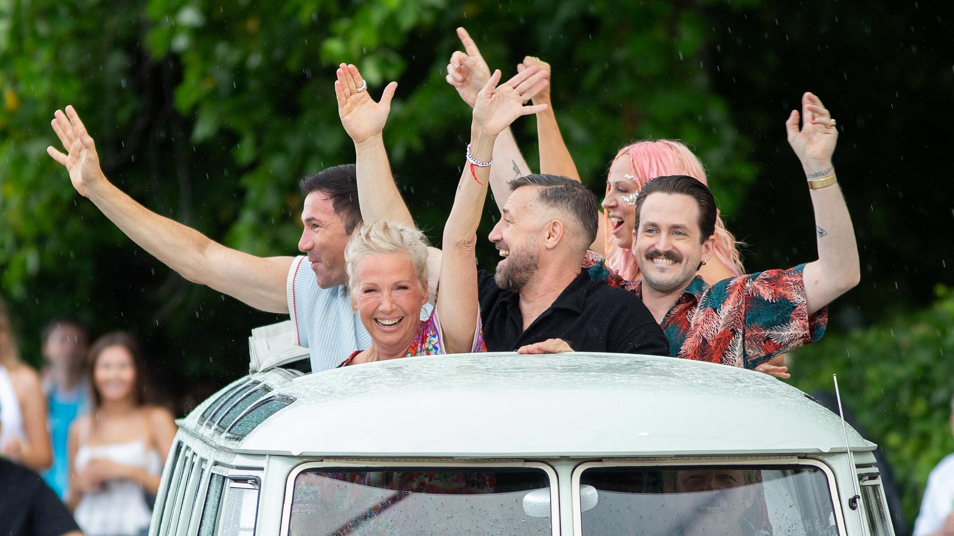 Opening der Urlaubs-Sendung: Die Moderatorin und einige Gäste schauen fröhlich winkend aus einem Autodach, während der Wagen einfährt.