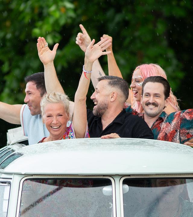 Opening der Urlaubs-Sendung: Die Moderatorin und einige Gäste schauen fröhlich winkend aus einem Autodach, während der Wagen einfährt.