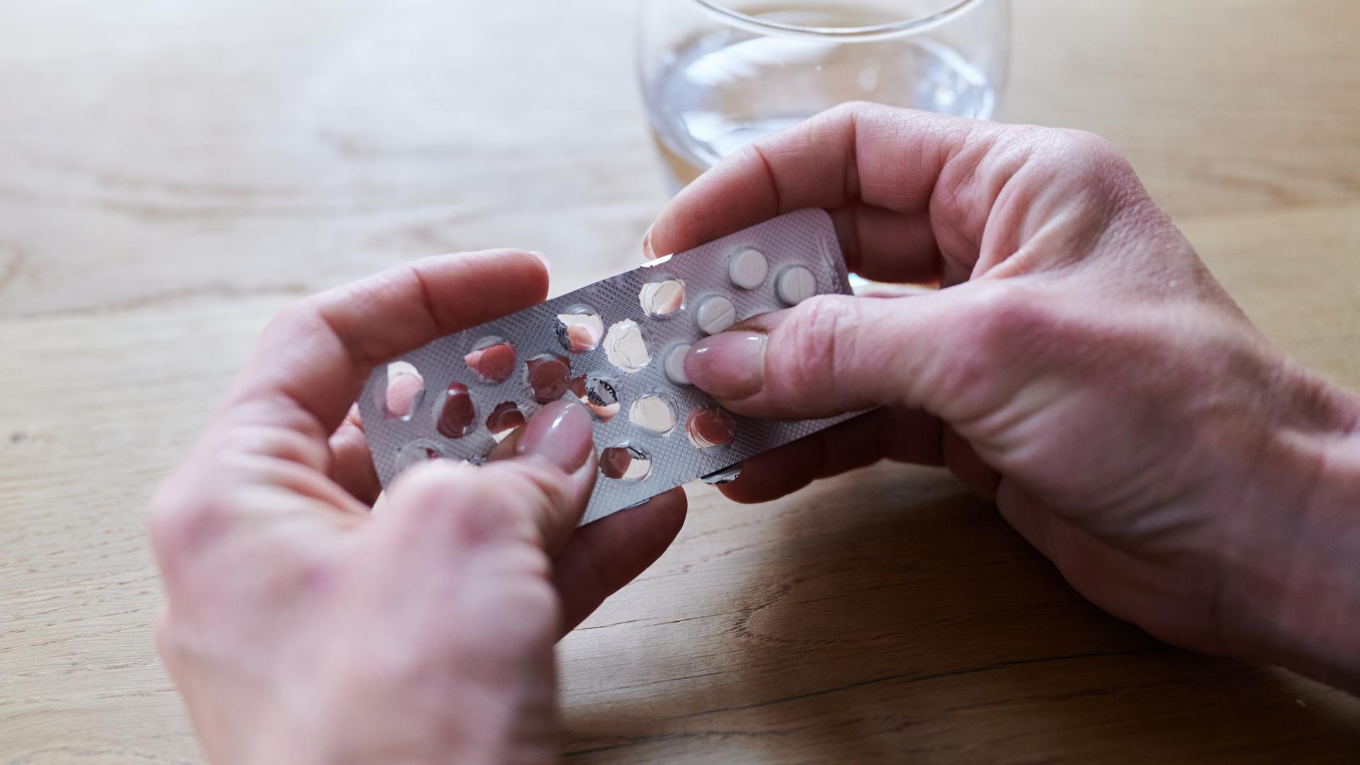 Eine Frau nimmt sich eine Tablette aus der Verpackung.