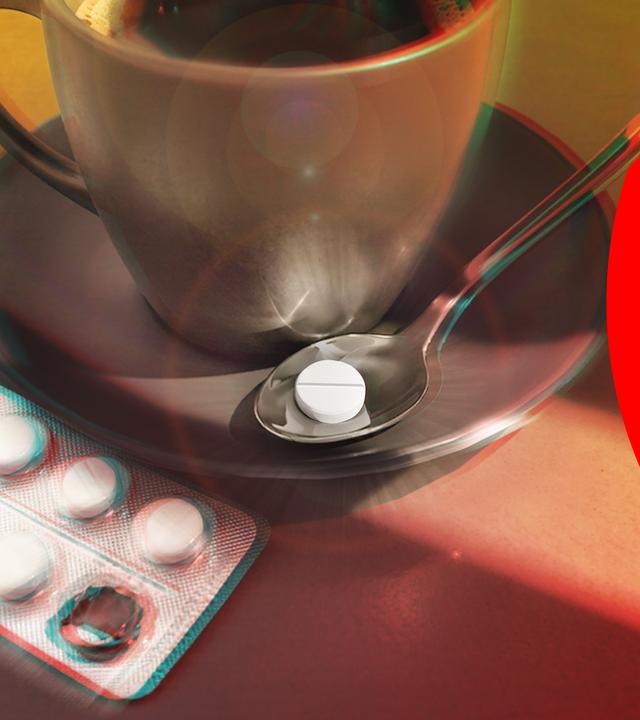 Eine Kaffeetasse steht auf einem Tisch. Daneben liegt auf der Untertasse ein Löffel, auf dem wiederum eine Tablette liegt. Neben der Untertasse ein Tablettenblister.