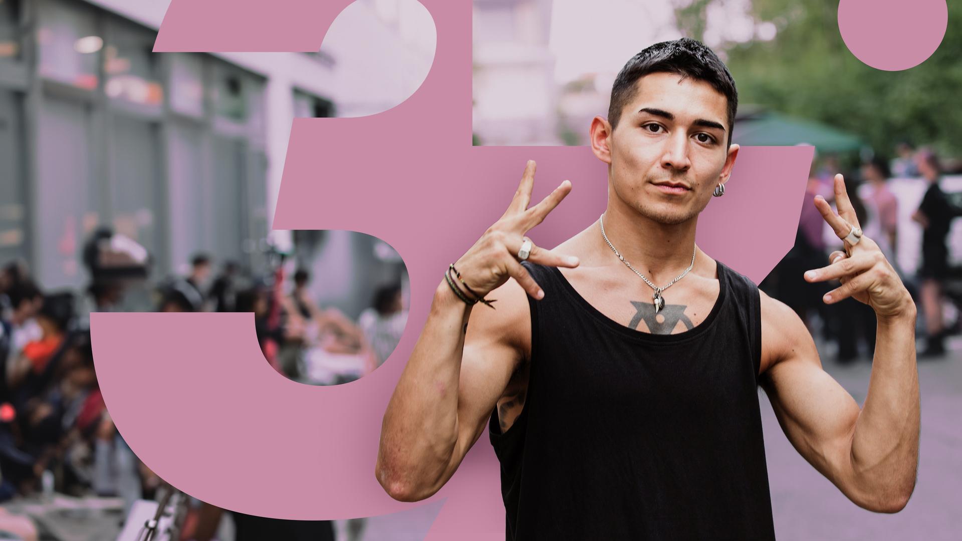 Ein junger Mann posiert auf der Straße, im Hintergrund, verschwommen zu erkennen, stehen einige Menschen beisammen