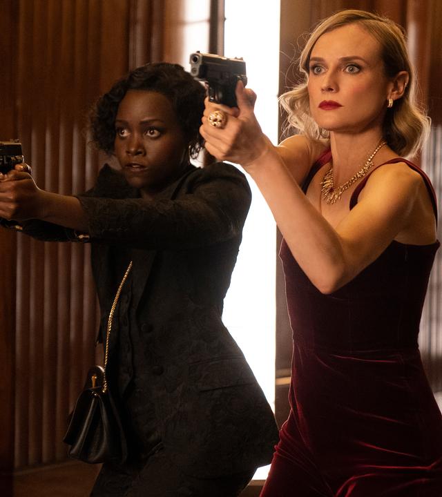 Khadijah (Lupita Nyong'o) und Marie (Diane Kruger) stehen mit gezogenen Pistolen in Abendgarderobe in einem Flur.