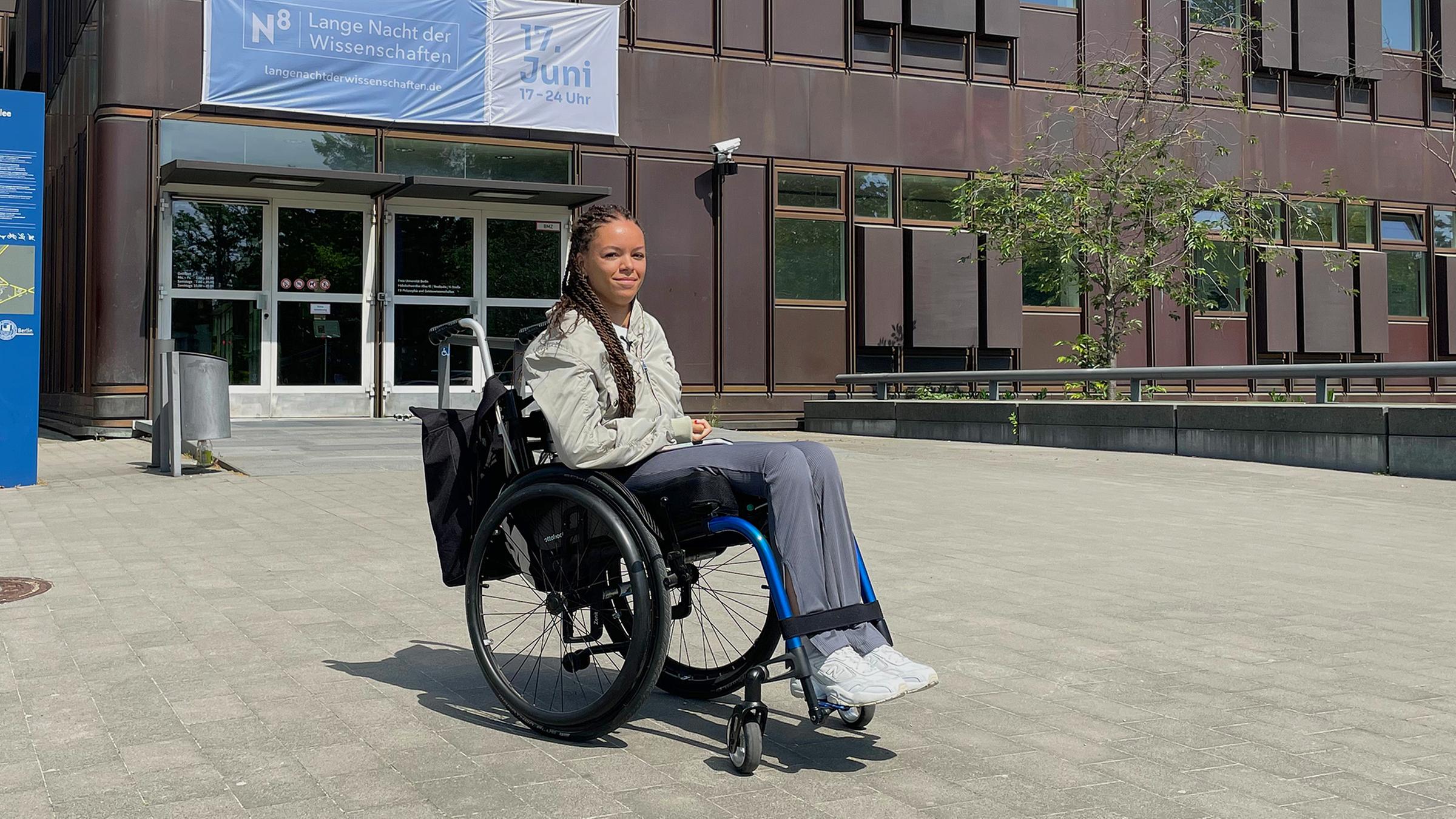 Elisa sitzt im Rollstuhl. Sie befindet sich vor der Freien Universität Berlin.