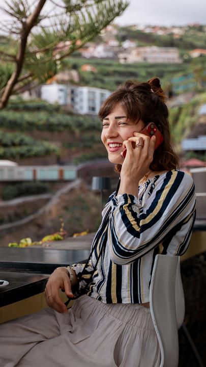 Freiberuflerin Nina hält lächelnd ein Smartphone in der Hand und telefoniert.