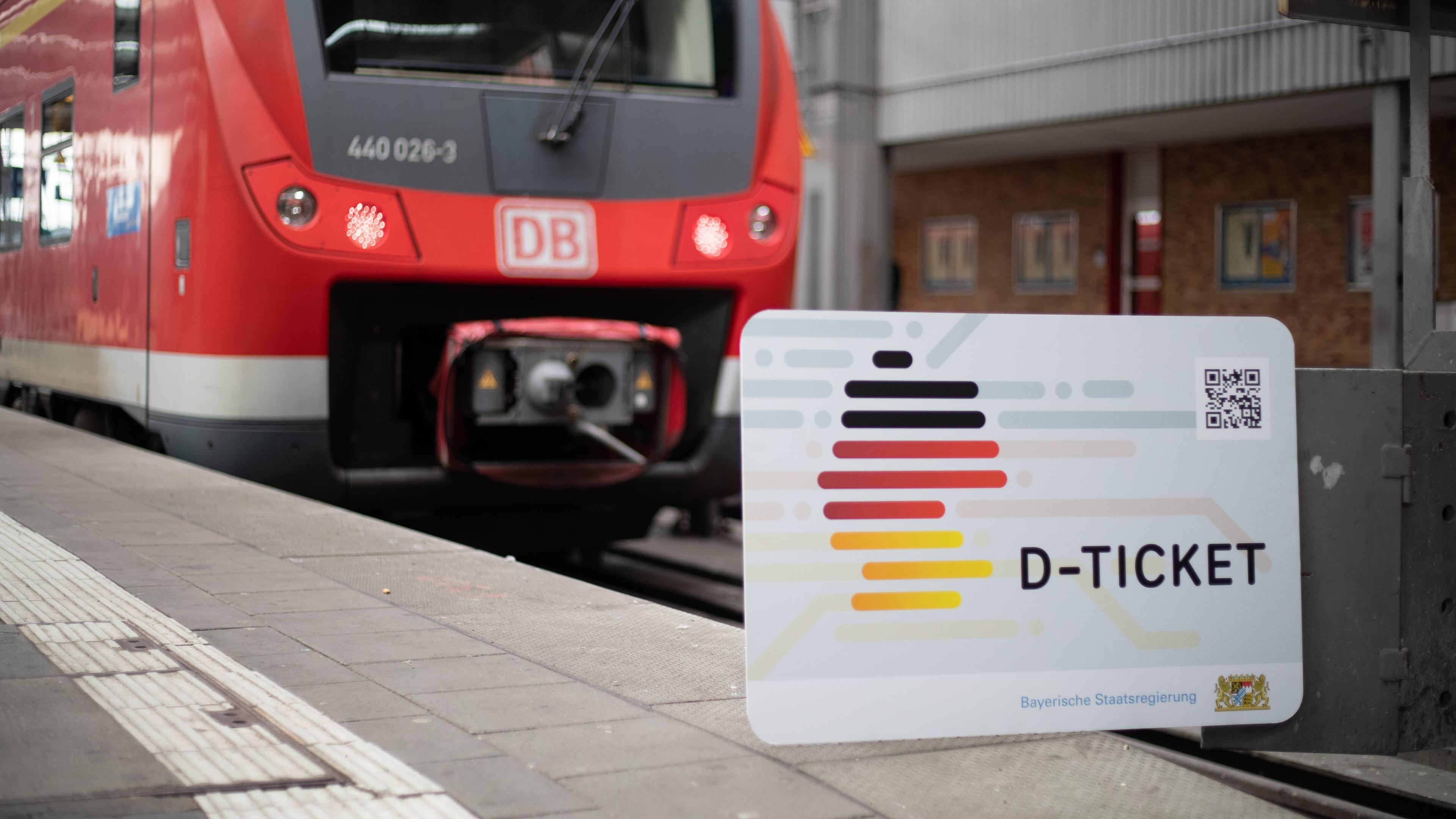 Ein übergroßes Deutschland-Ticket ist vor eine Regionalbahn in einem Bahnhof montiert