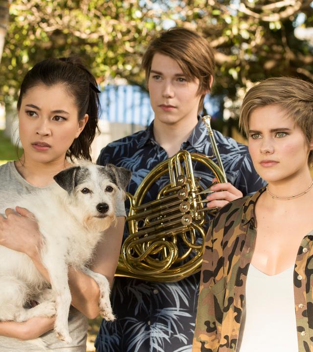 Kyra, Darra und Imogen schauen verwirrt. Kyra hat einen Hund auf dem Arm.