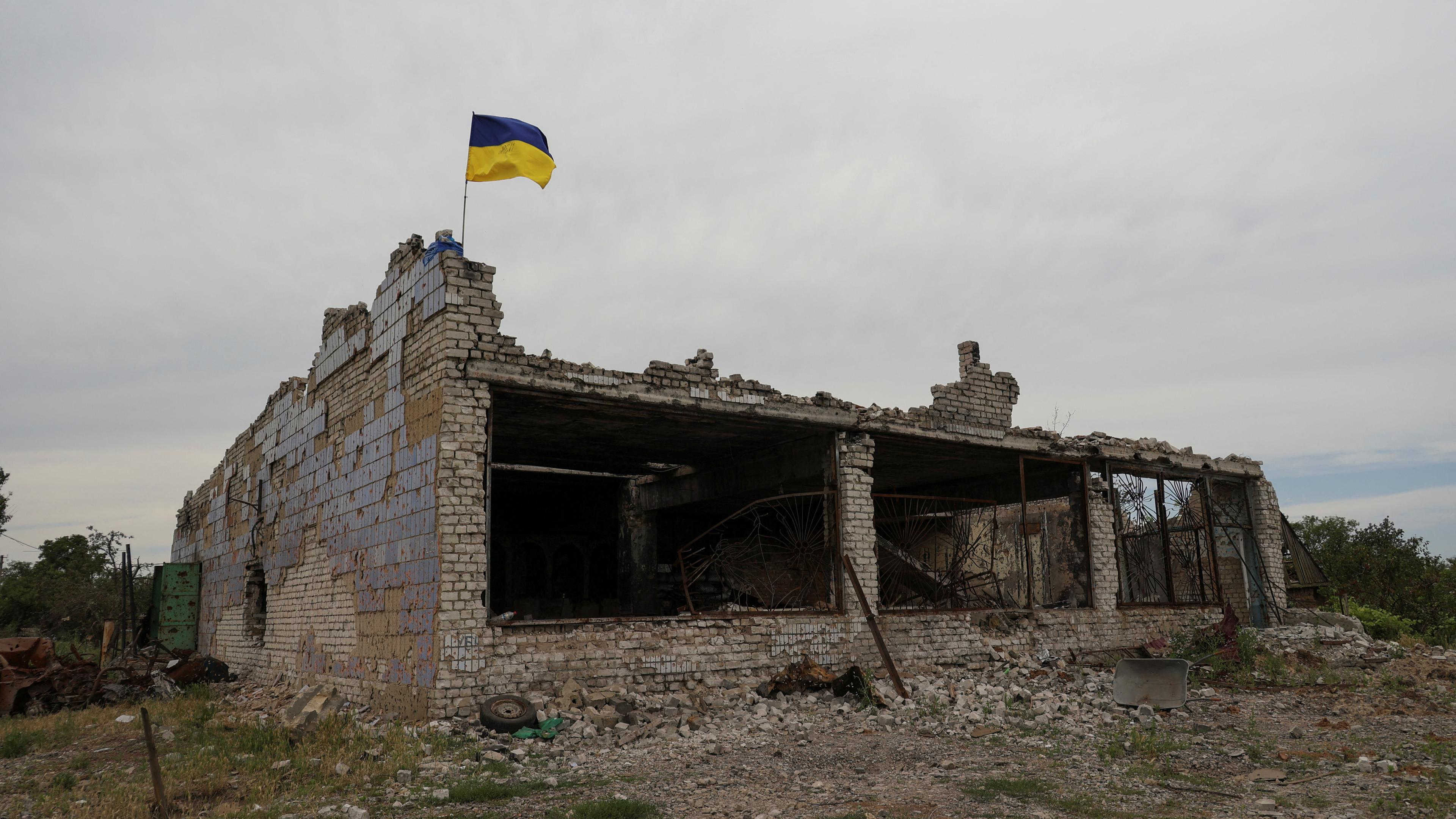 Zu sehen ist ein zerstörtes Gebäude mit einer Ukraine-Flagge.