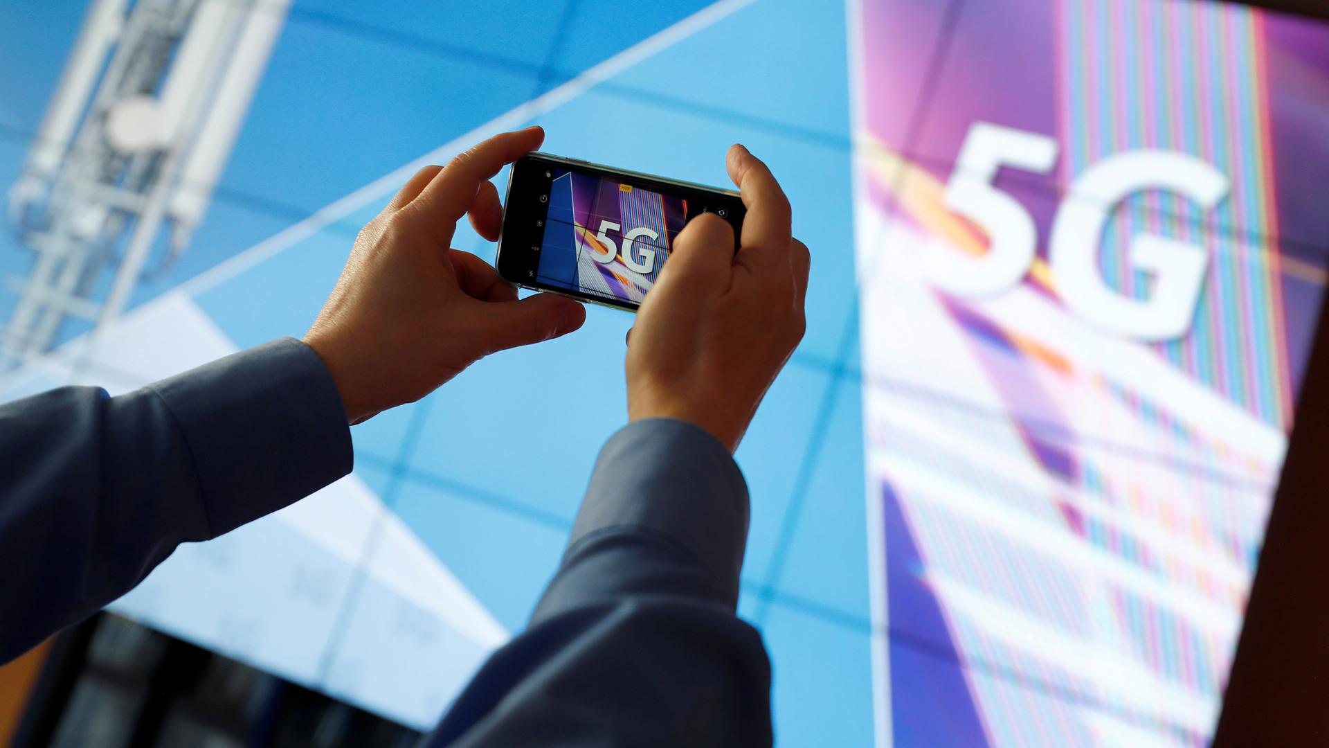 Ein Journalist macht mit seinem Smartphone ein Foto von dem 5G-Logo in Mainz am 19.03.2019