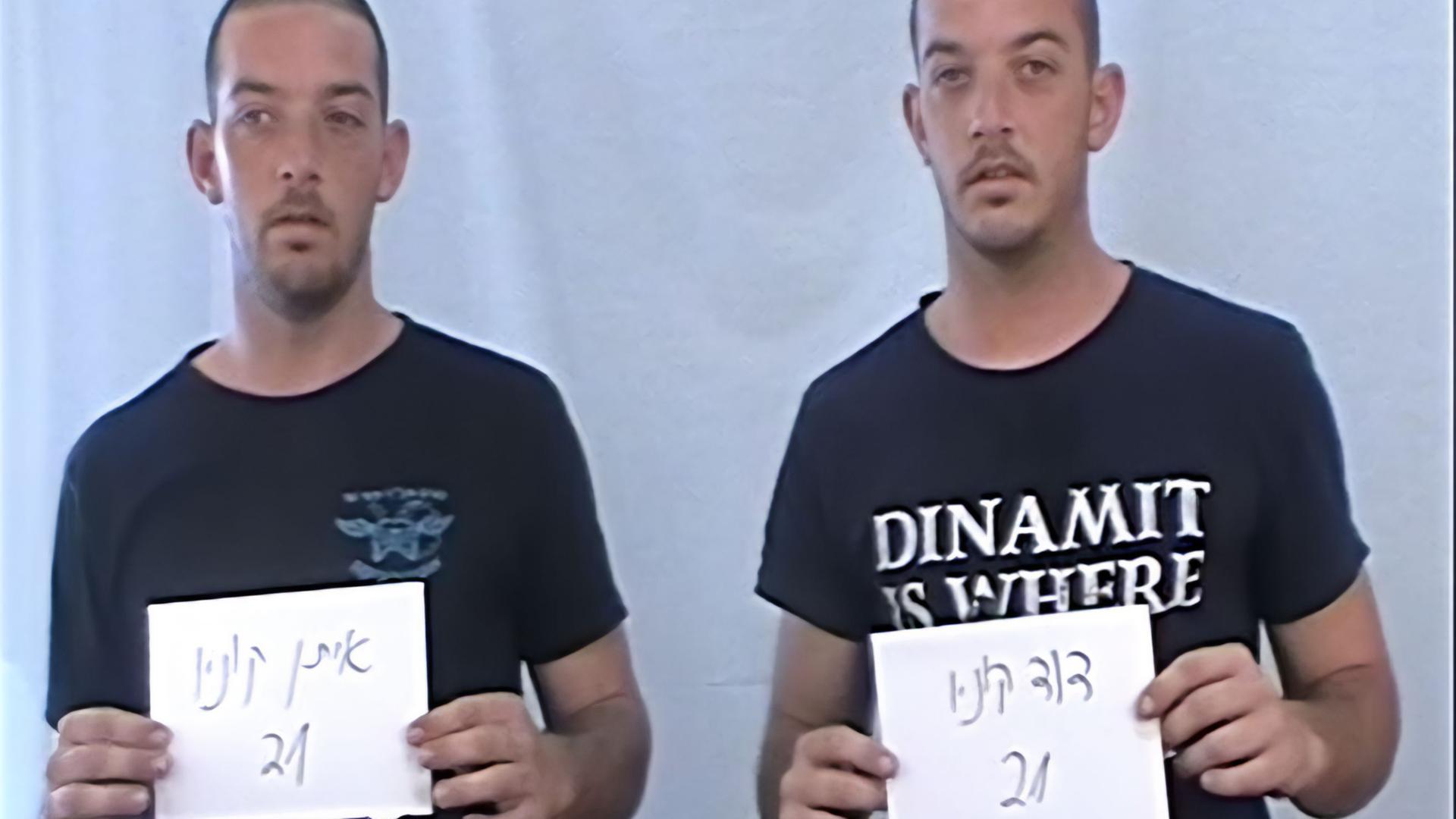 Zwei gleich aussehende Zwillings-Männer in T-Shirts stehen nebeneinander und halten Zettel mit Nummern hoch.