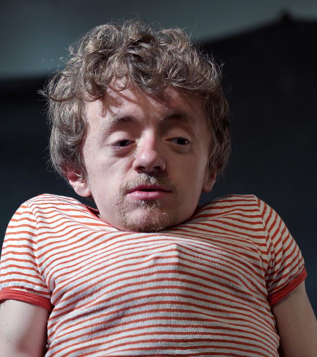 Leonard, ein kleinwüchsiger junger Mann, trägt ein rotgestreiftes T-Shirt.