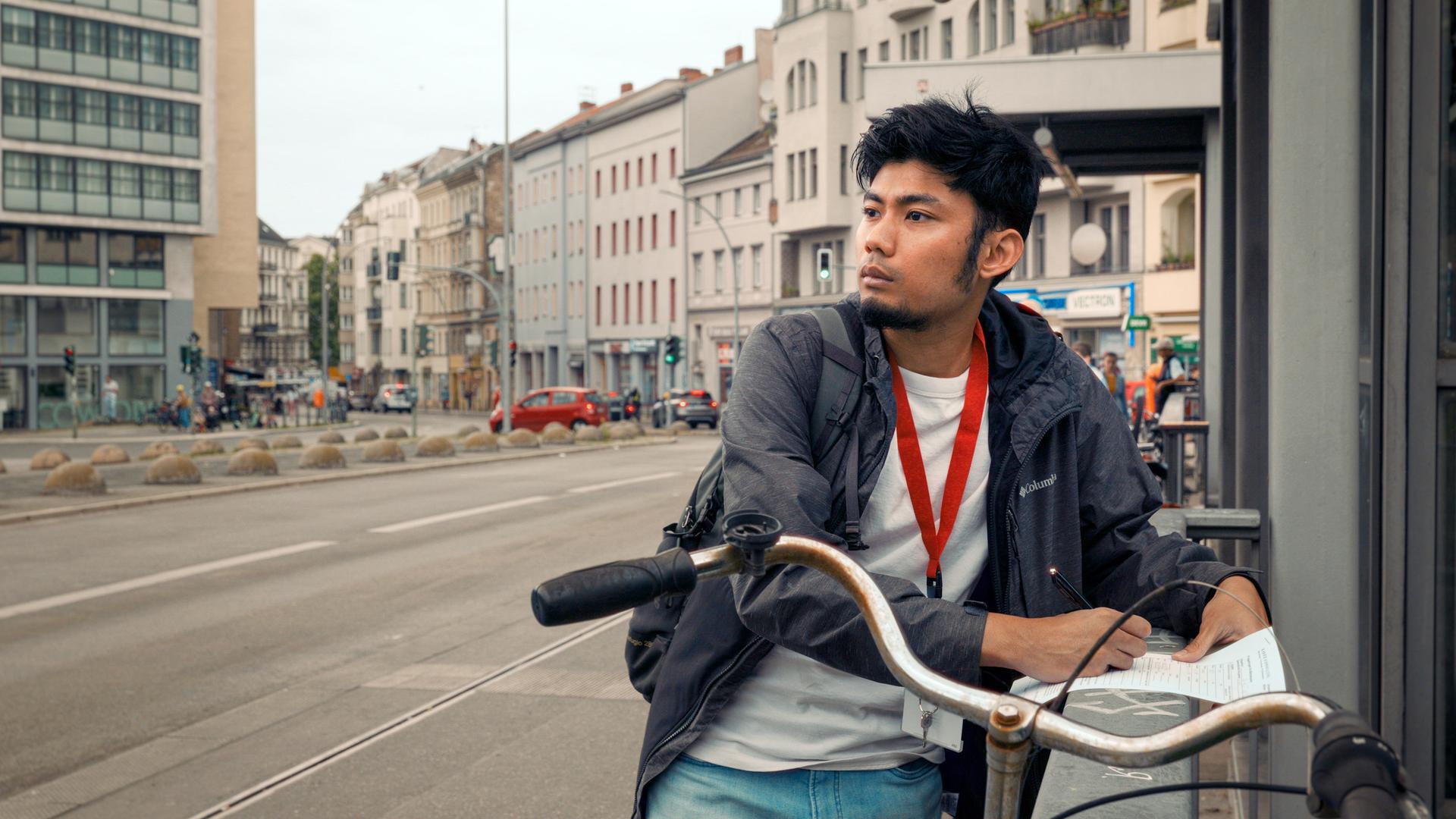 Junger Mann steht an einem Geländer und macht sich auf einem Blatt Papier Notizen.