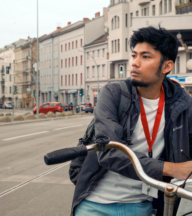 Junger Mann steht an einem Geländer und macht sich auf einem Blatt Papier Notizen.