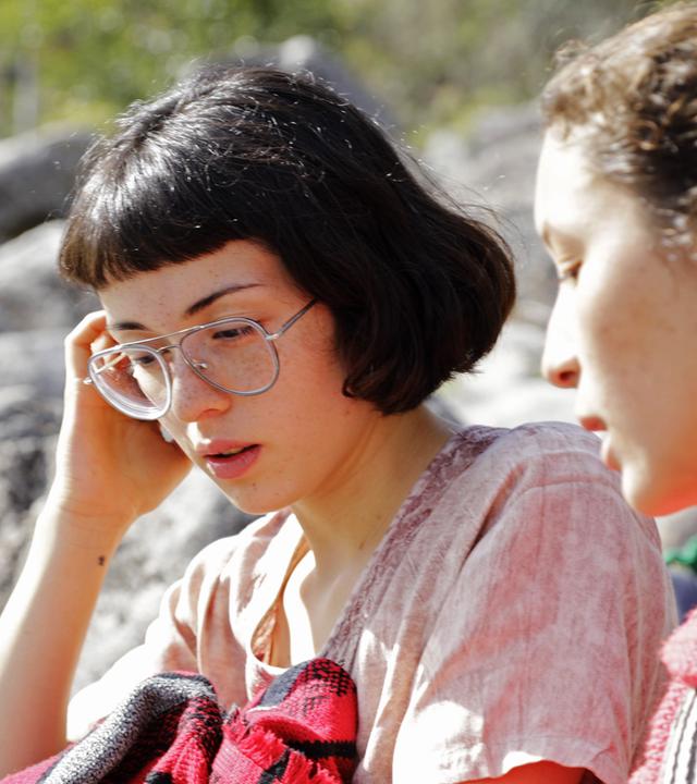 "Ab 18! Die Tochter von": Zwei dunkelhaarige Mädchen sitzen gemeinsam am Ufer eines Flusses.