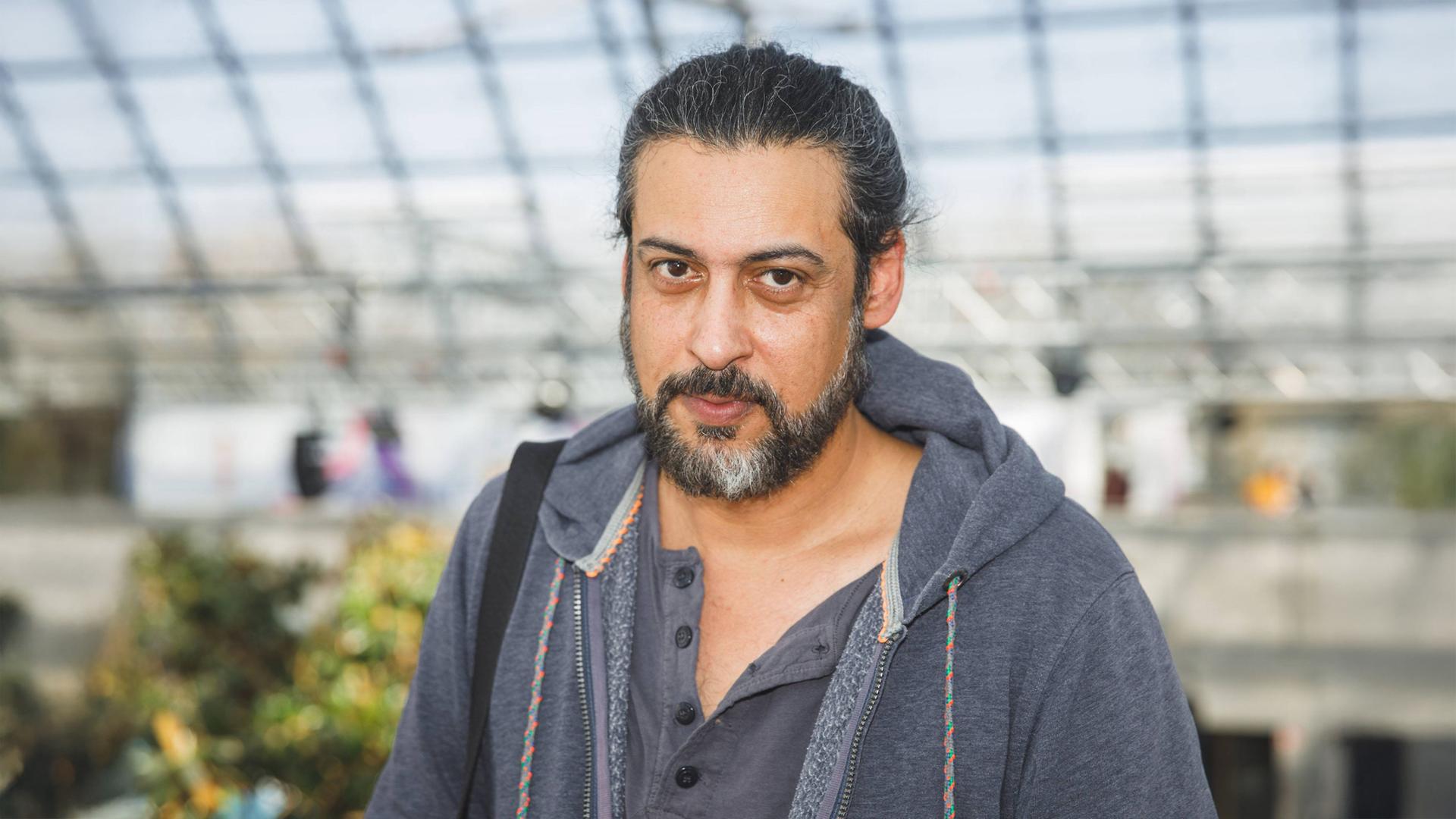 Porträtfoto eines Mannes mit zurückgebundenen graumelierten Haaren und Bart.