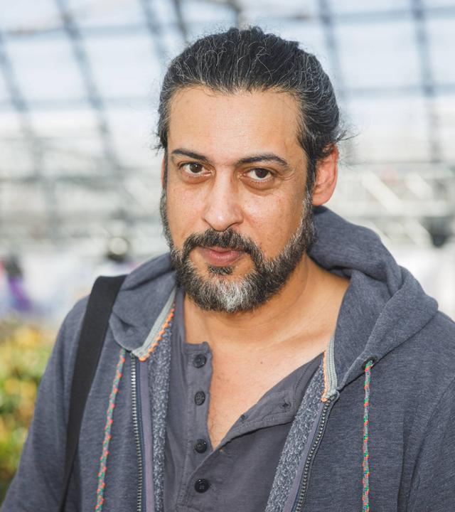 Porträtfoto eines Mannes mit zurückgebundenen graumelierten Haaren und Bart.