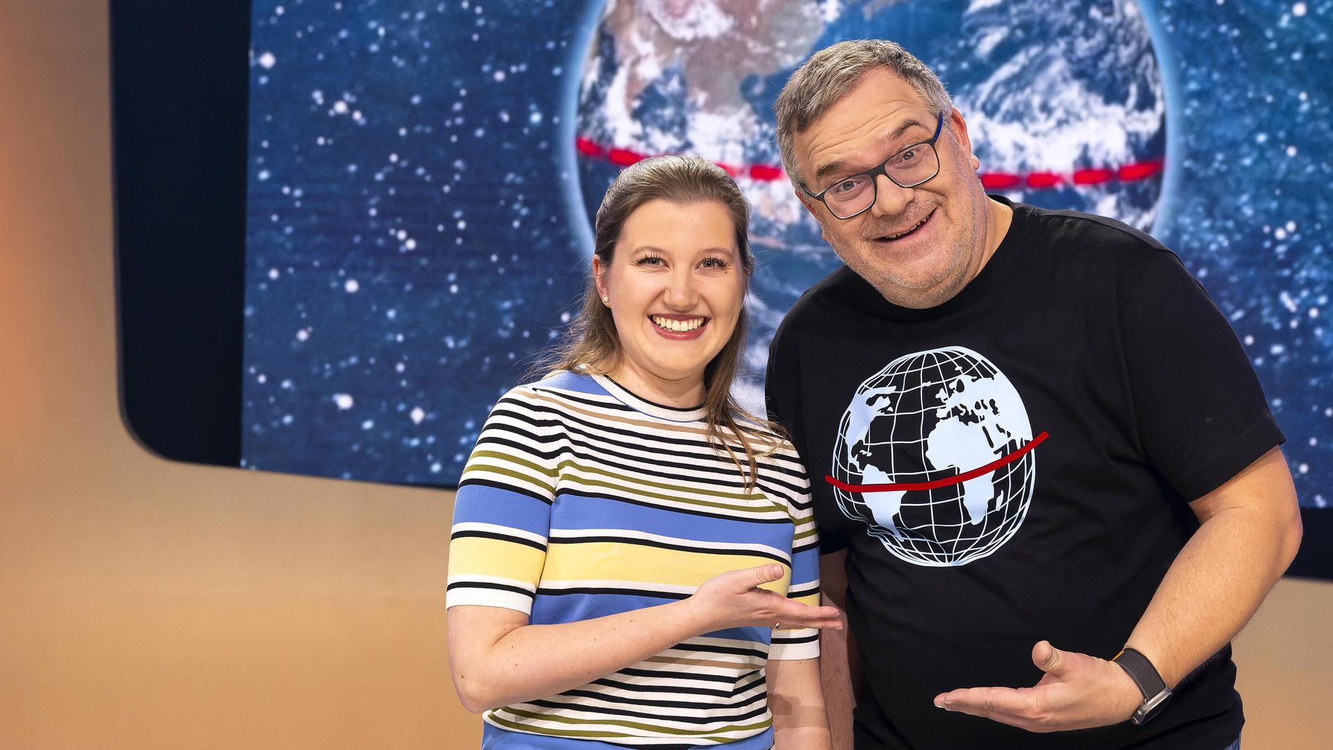 Meteorologin Leonie Imhäuser steht neben Elton im Studio. Beide zeigen mit den Händen aufeinander und lächeln.