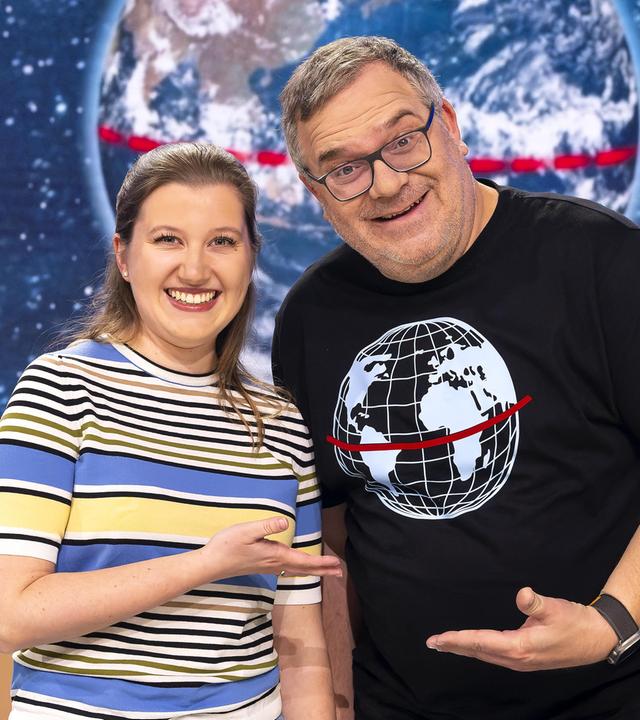 Meteorologin Leonie Imhäuser steht neben Elton im Studio. Beide zeigen mit den Händen aufeinander und lächeln.