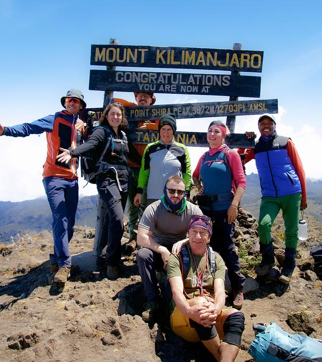 Acht Personen in Trekkingausrüstung posieren am Gipfel des Kilimandscharo für ein Gruppenfoto