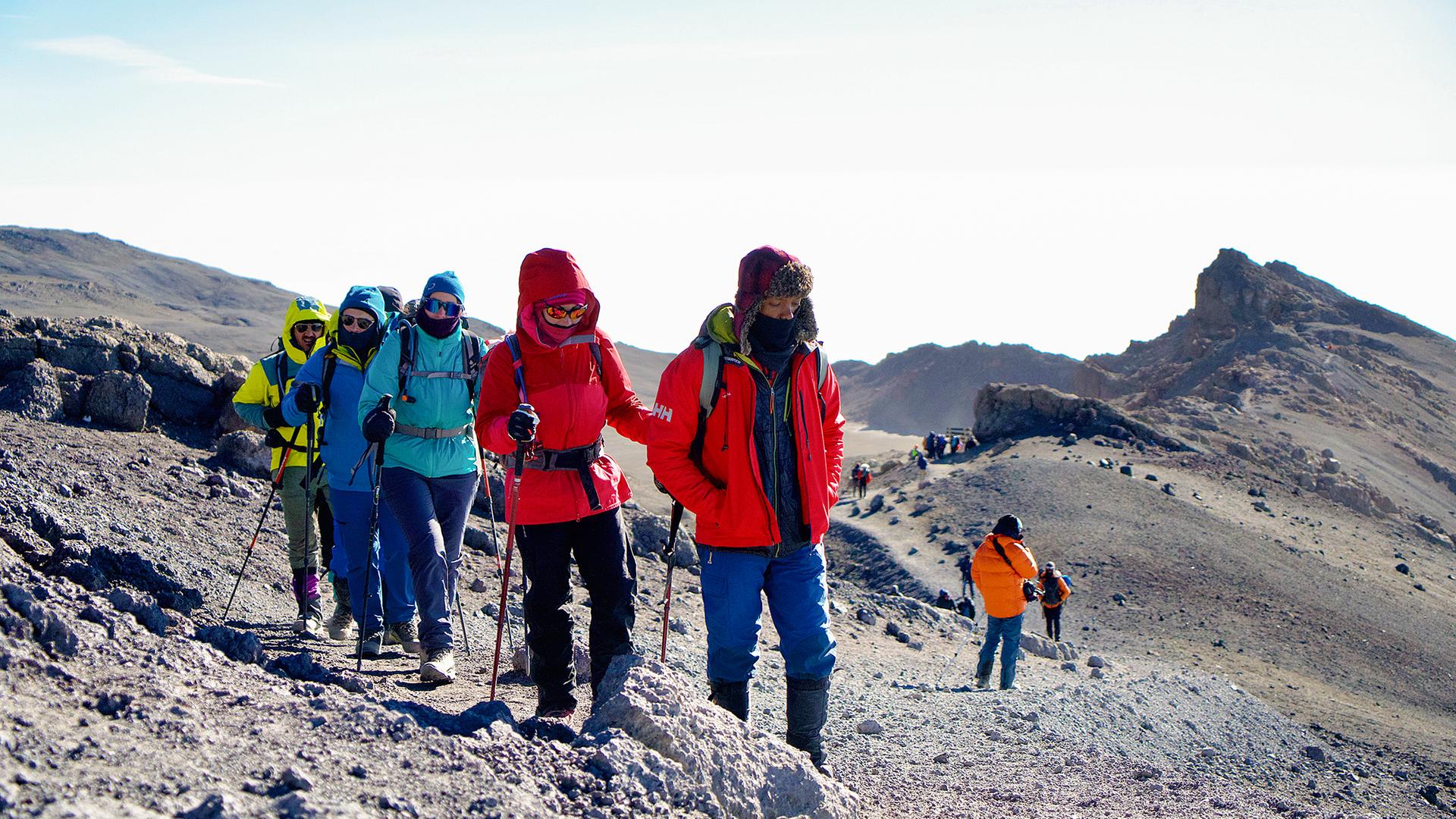 Warm gekleidete Wandergruppe im Gänsemarsch mit Trekkingstöcken auf einem kargen Weg.