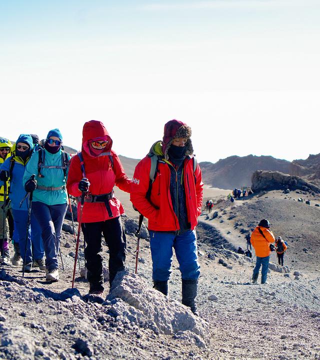 Warm gekleidete Wandergruppe im Gänsemarsch mit Trekkingstöcken auf einem kargen Weg.