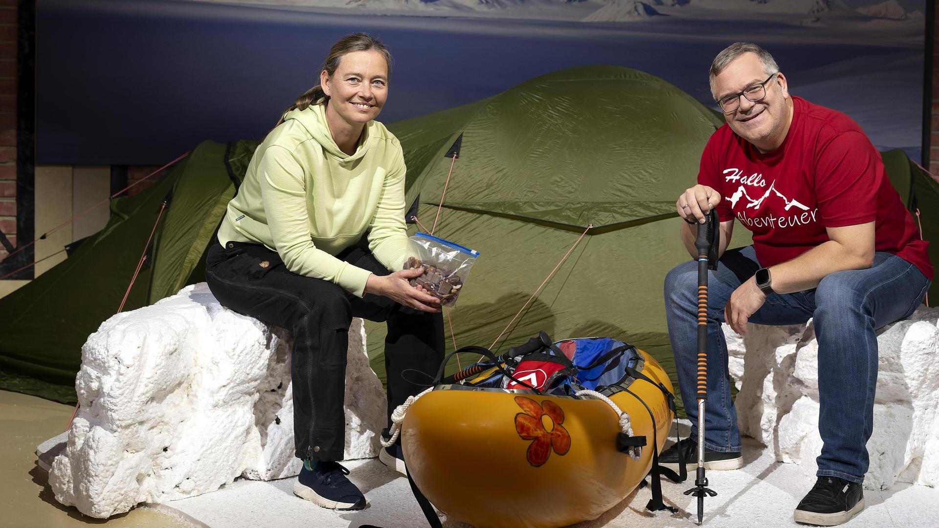 "1, 2 oder 3 - Abenteuerinnen": Birgit Lutz und Elton sitzen im Studio vor einem Zelt auf nachgebauten Eisblöcken. Zwischen ihnen steht ein Kanu.