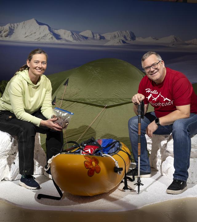 "1, 2 oder 3 - Abenteuerinnen": Birgit Lutz und Elton sitzen im Studio vor einem Zelt auf nachgebauten Eisblöcken. Zwischen ihnen steht ein Kanu.