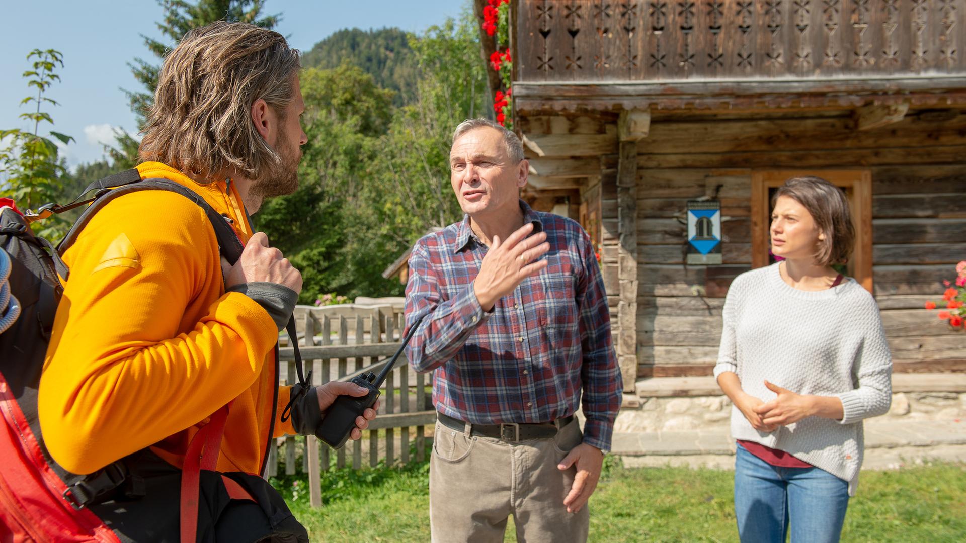 Vor dem Haus stehen Bruno Steyer (Franz Froschauer) und Mona (Nina Steils) dem Bergretter Markus Kofler (Sebastian Ströbel) gegenüber. 