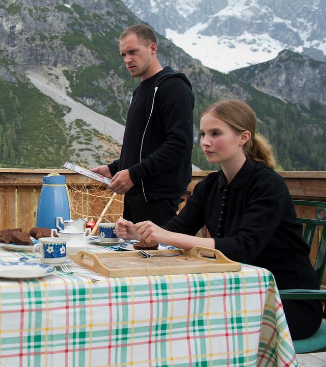 "Die Bergretter - Achillesferse (1)": Joseph Binder (Paul Matic) und seine Kinder Marc (Lorenz Weh) und Melanie (Annika Schrumpf) sitzen auf der Terrasse am gedeckten Kaffeetisch. Daneben steht sein Sohn Philipp (Kai Malina). Die Kinder schauen traurig zu ihrem Vater, der mit gefalteten Händen ins Leere starrt. Im Hintergrund sind die Berge zu sehen.