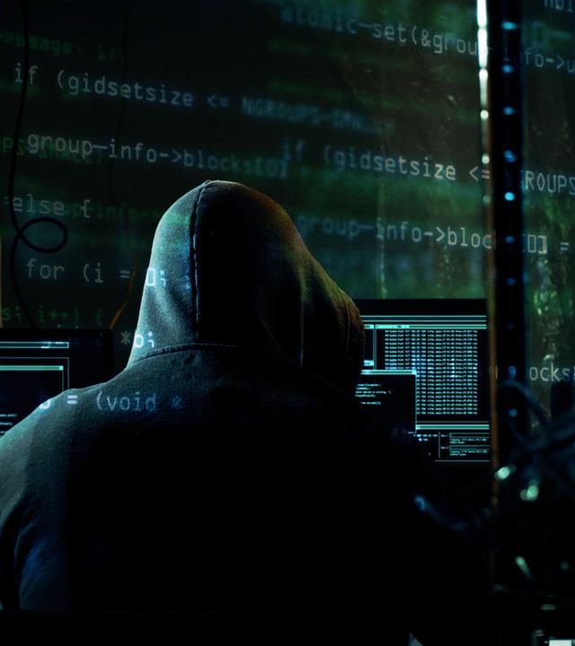 "Achtung, Geldfallen! - Die Tricks der Finanzabzocker": In einem abgedunkelten Raum sitzt ein Mensch vor mehreren Monitoren. Er trägt einen dunklen Kapuzenpulli und ist nur von hinten zu sehen.