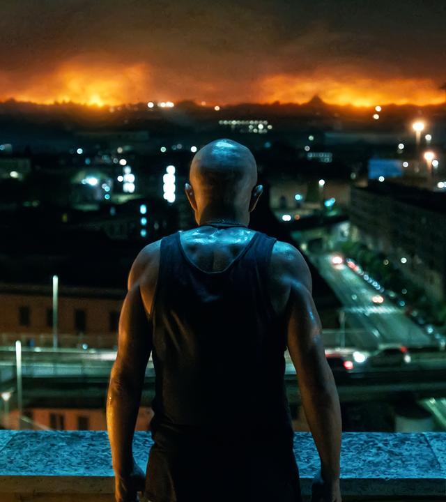 Cammello (Pierfrancesco Favino) steht mit dem Rücken zur Kamera vor einer brennenden Stadt.