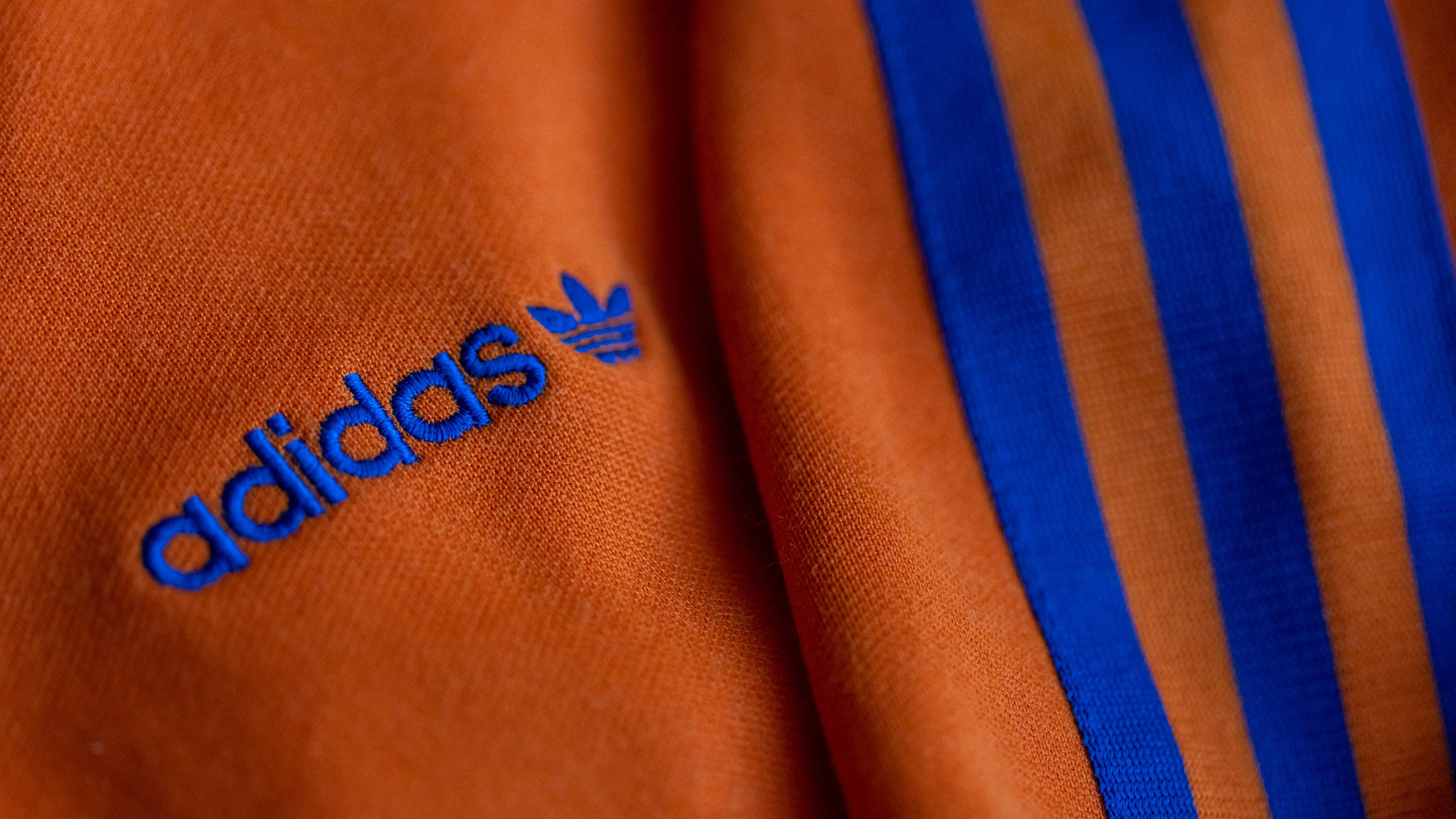 Bayern, Herzogenaurach: Das Logo des Sportartikelherstellers adidas in blau auf einer orangen Jacke.