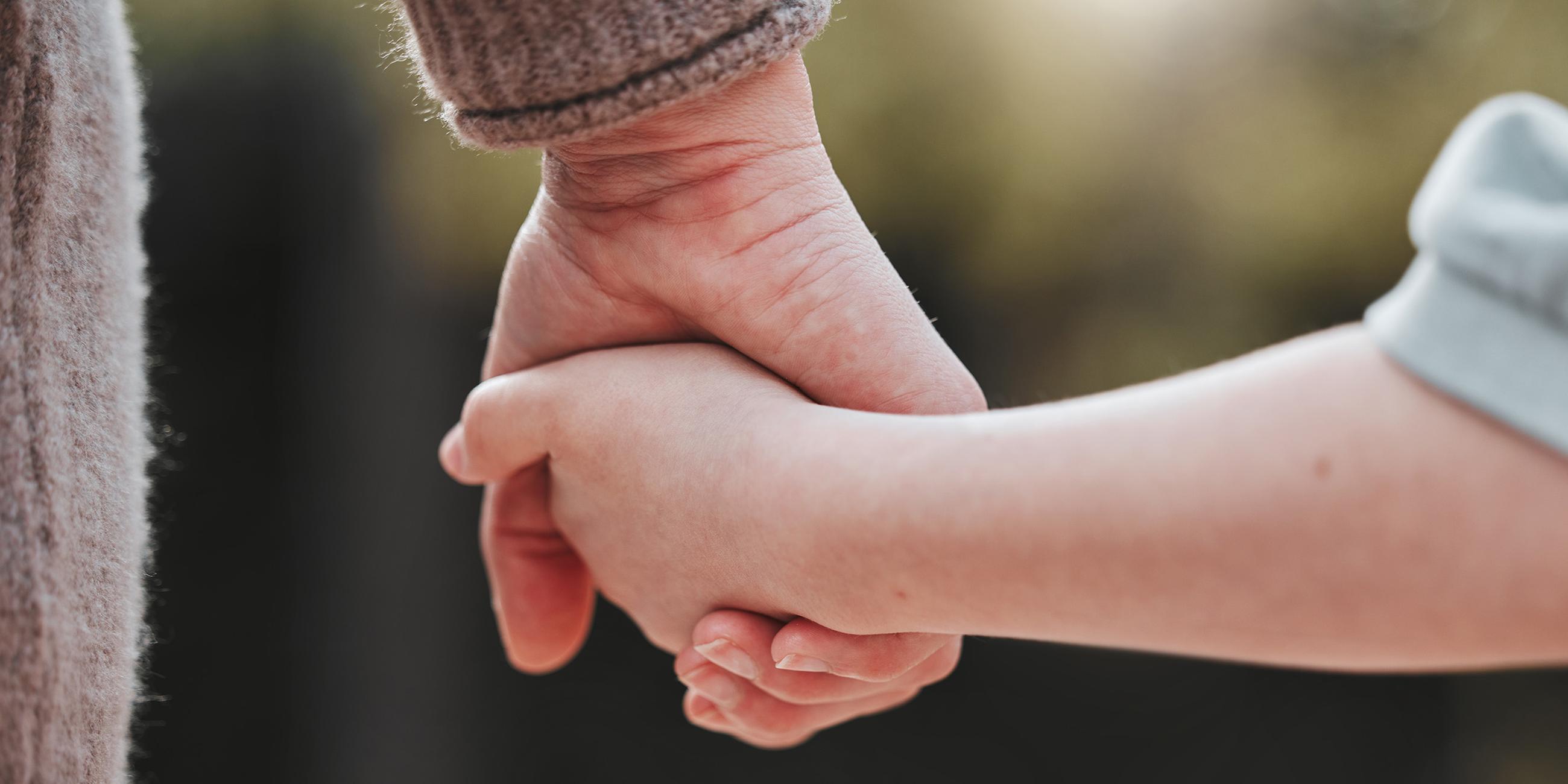 Ein Elternteil hält die Hand ihres Kindes. 