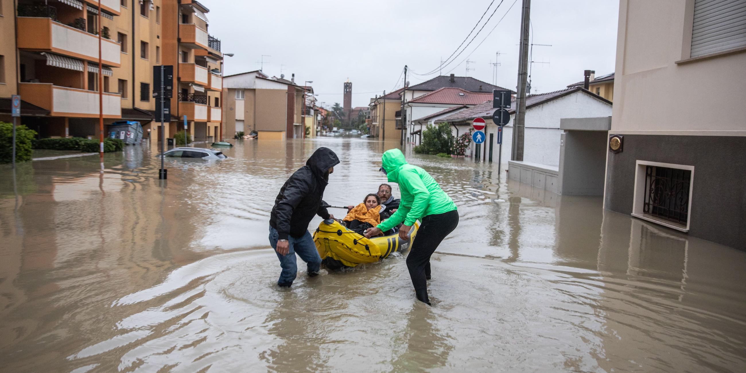 Zwei Männer ziehen Schlauchboot hinter sich her bei Hochwasser in Norditalien