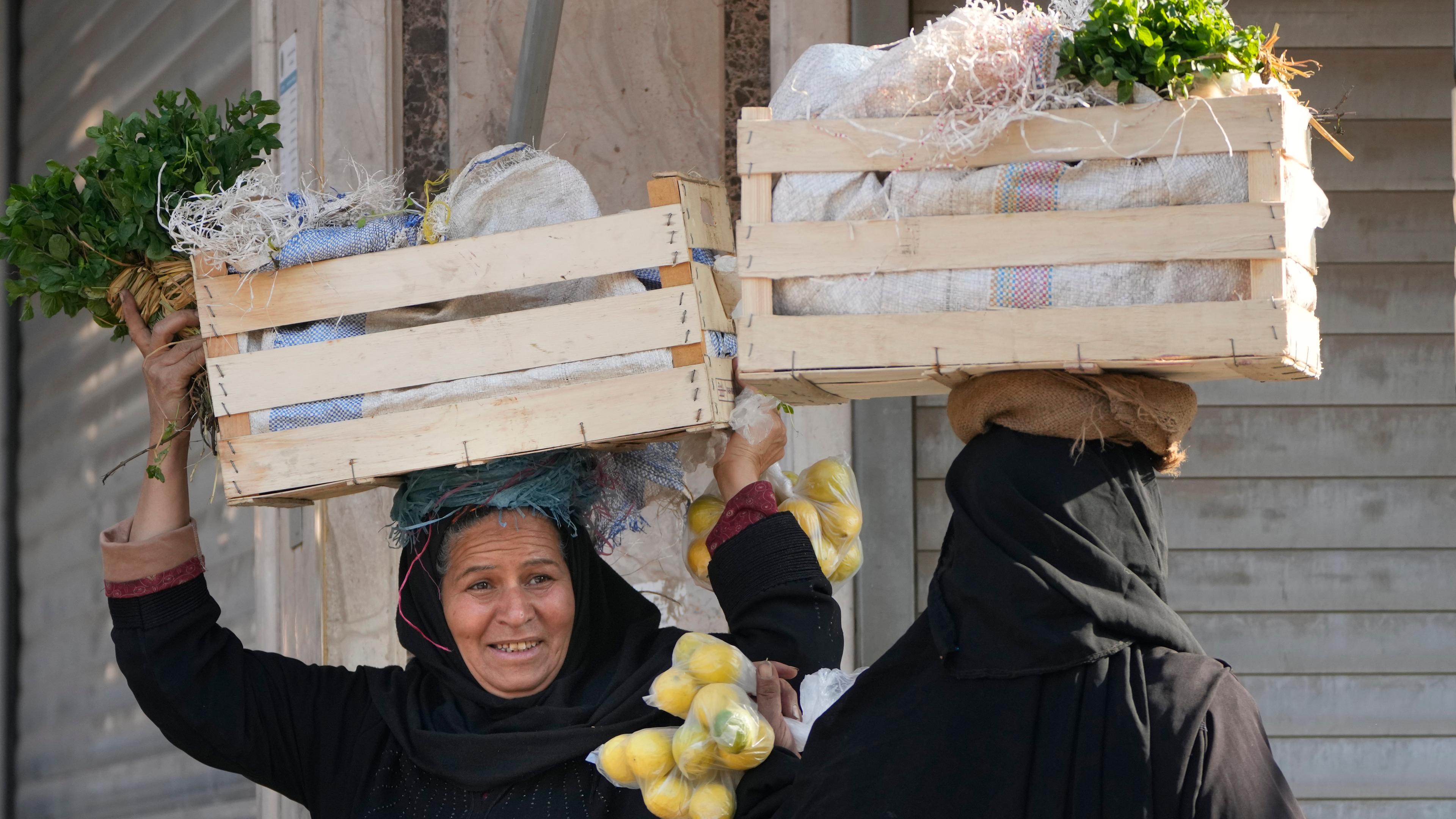 Zwei verschleierte Frauen tragen Kisten mit Gemüse auf dem Kopf; Kairo, Ägpyten; 26.01.2023