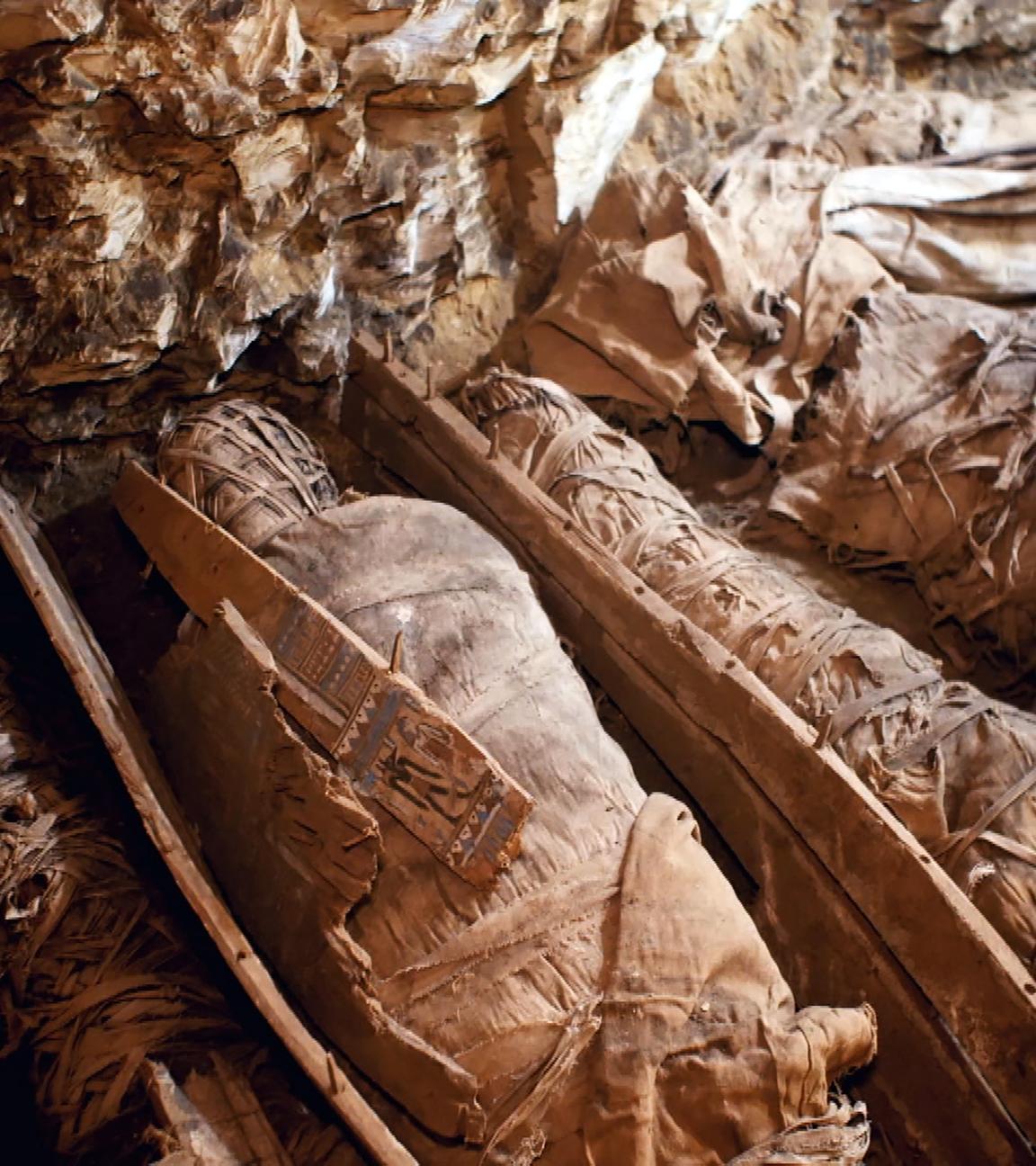 Sechs eingewickelte Mumien liegen eng beieinander auf dem Boden einer Grabkammer.