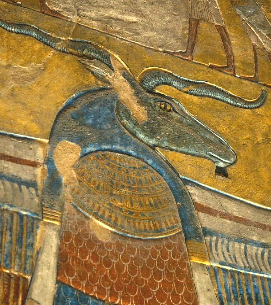 Eine Detailansicht einer Wandmalerei zeigt das Bild des Gottes Chnum. Sein Kopf ist blau und gleicht dem eines Widders. Er hat Hörner, die nach links und rechts zeigen.