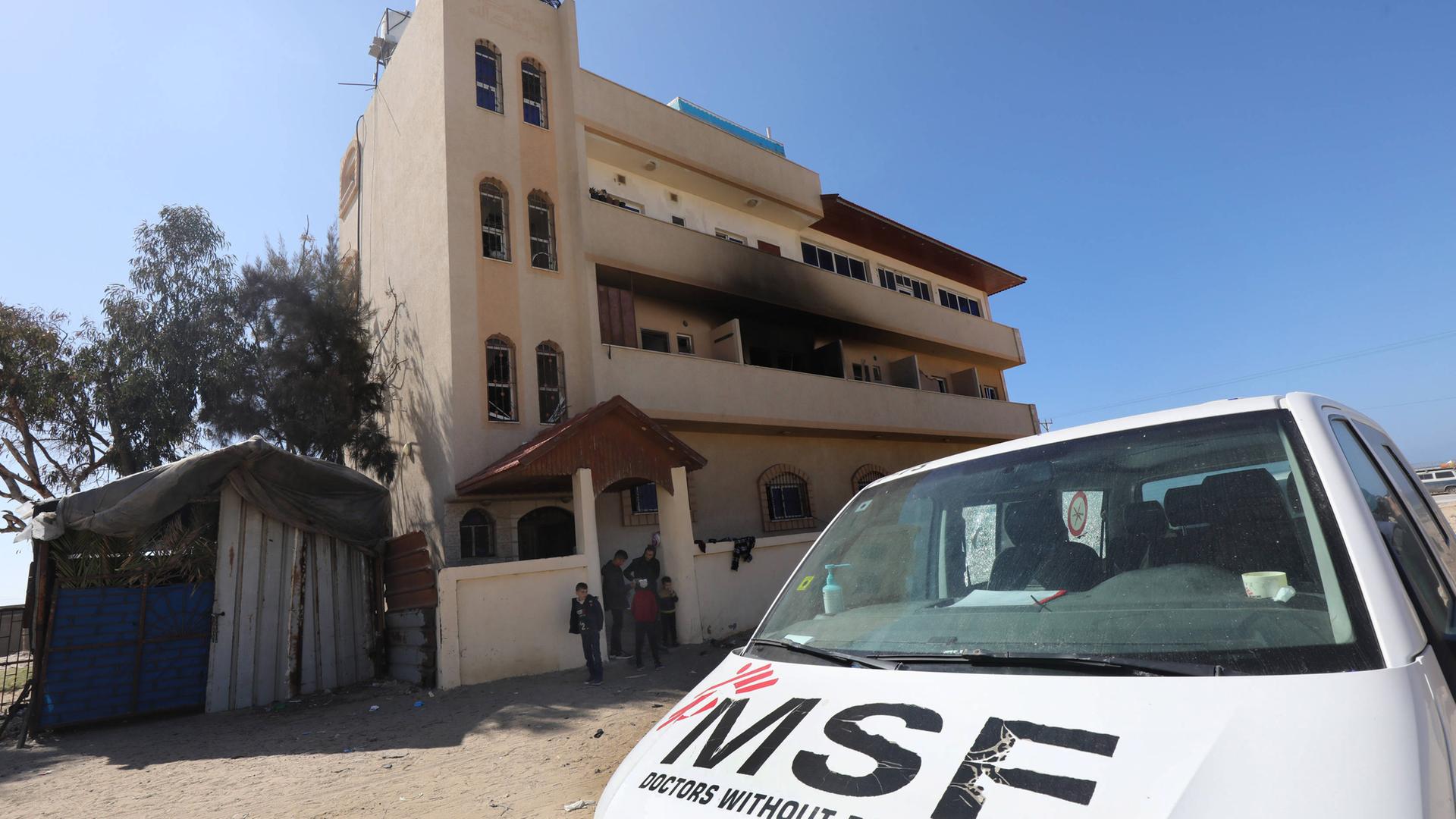 Vor einem dreistöckigen Haus mit einem rußgeschwärzten Balkon steht ein weißer Lieferwagen der Ärzte ohne Grenzen.