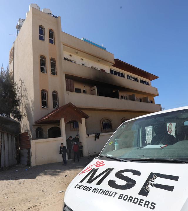 Vor einem dreistöckigen Haus mit einem rußgeschwärzten Balkon steht ein weißer Lieferwagen der Ärzte ohne Grenzen.