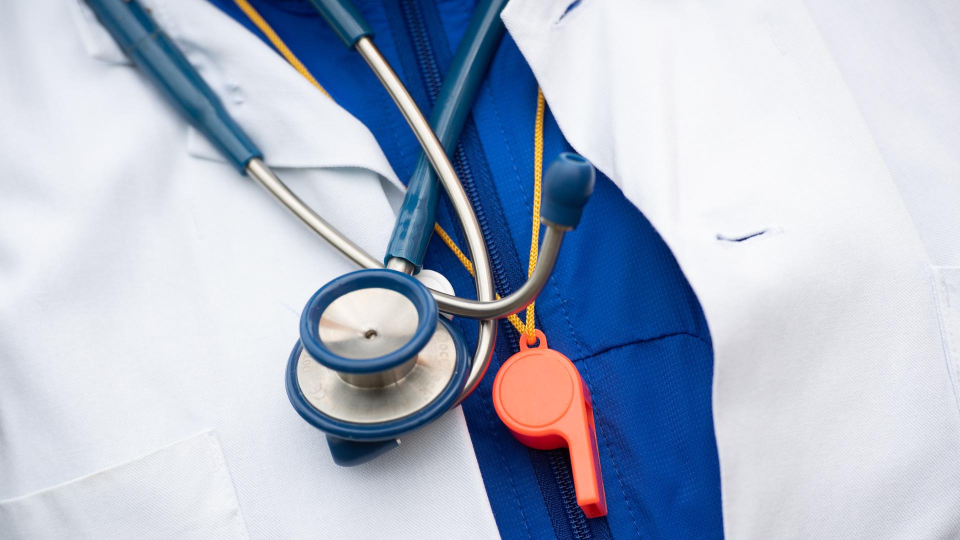  Ein Mann nimmt an einer Demonstration von hunderten Ärzte und Ärztinnen teil, die mehr Geld und die Sicherung ihres Tarifvertrages fordern, dabei trägt er ein Stethoskop und eine Trillerpfeife um den Hals.