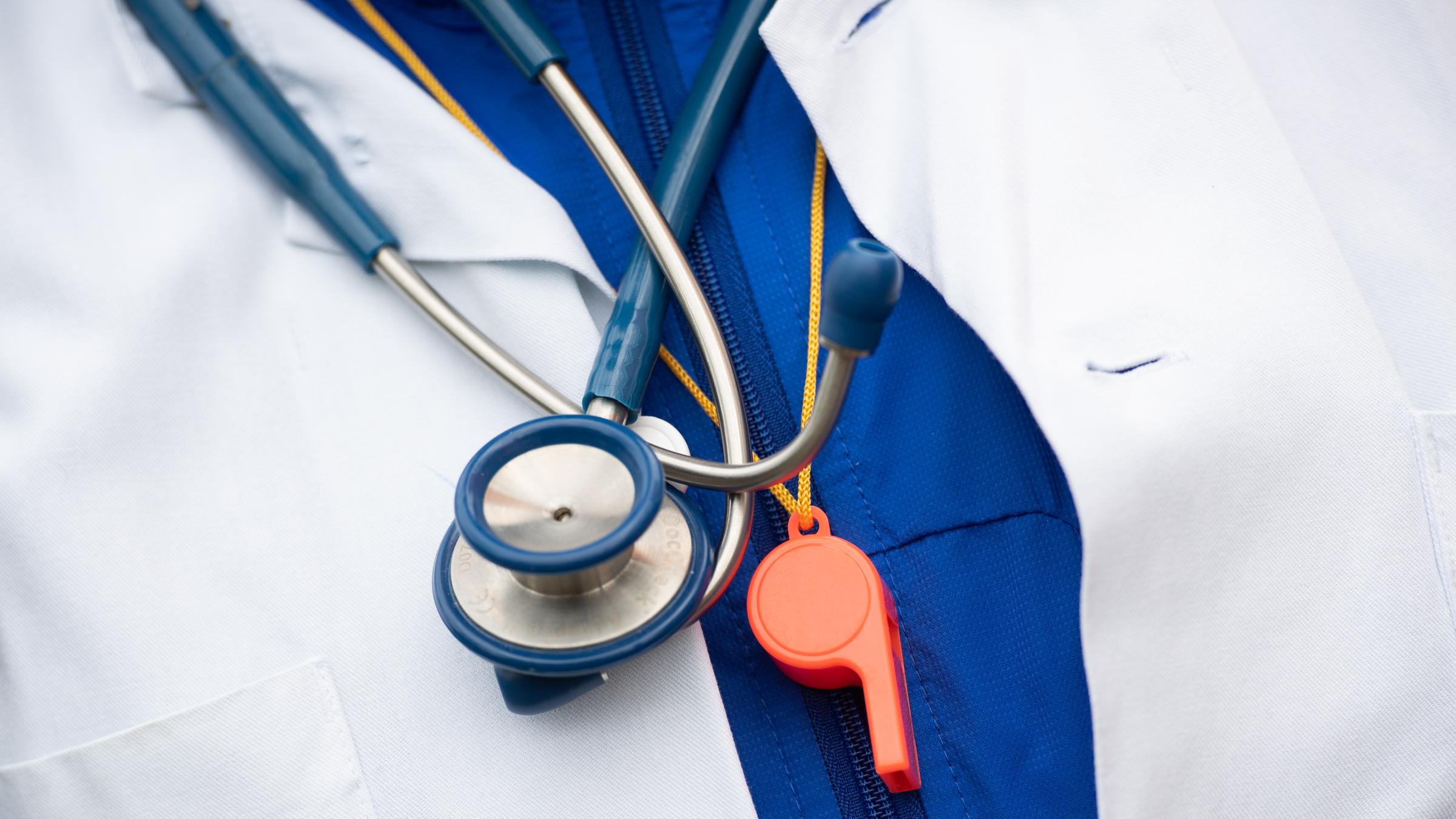  Ein Mann nimmt an einer Demonstration von hunderten Ärzte und Ärztinnen teil, die mehr Geld und die Sicherung ihres Tarifvertrages fordern, dabei trägt er ein Stethoskop und eine Trillerpfeife um den Hals.