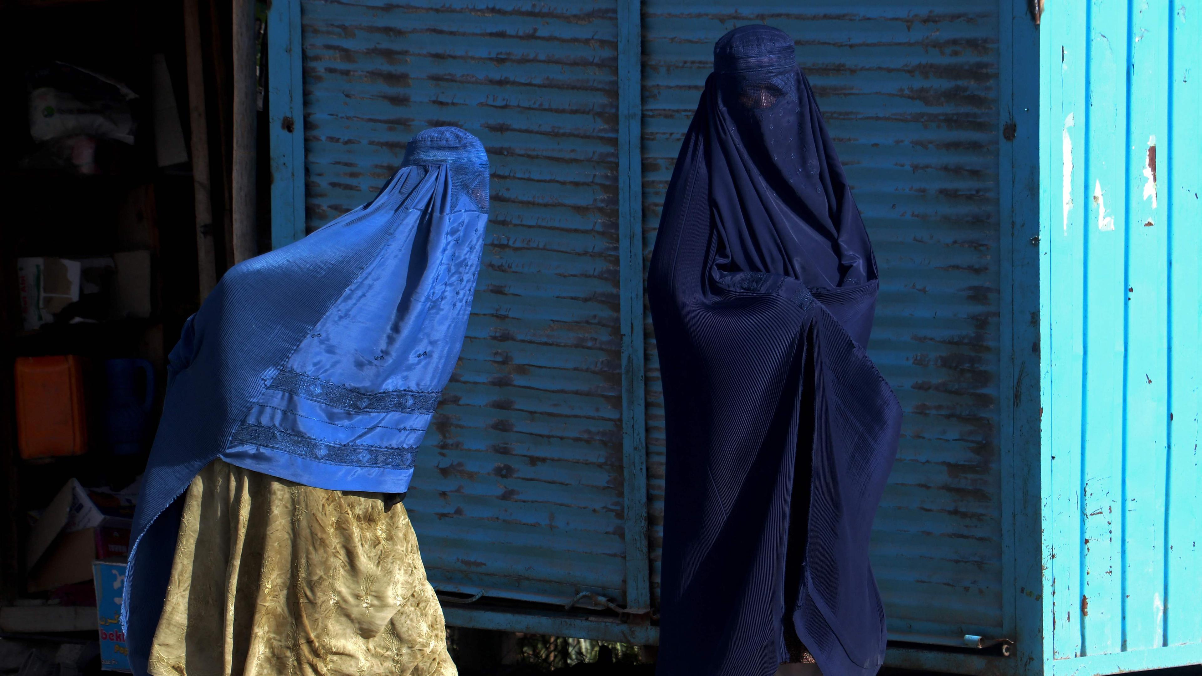 Zwei Frauen in Burka gehen vor einer Mauer