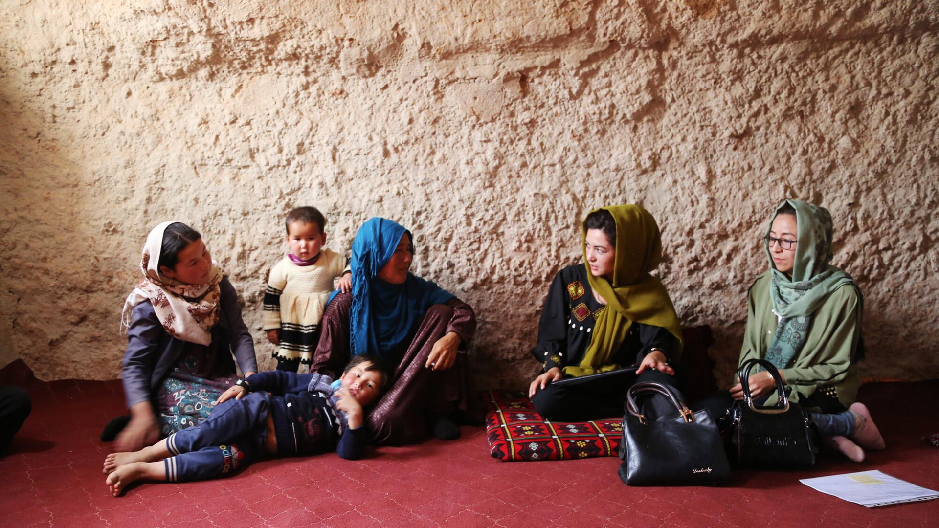 Islamic Relief-Mitarbeiterinnen sitzen mit afghanischen Müttern und ihren Kindern in einem Raum auf dem Boden.