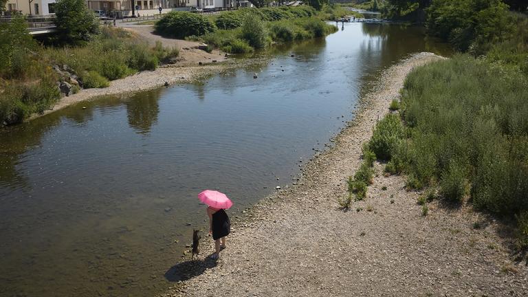 Eine Frau geht bei heißem Wetter im Ahrtal am Ufer der Ahr mit einem Hund spazieren.