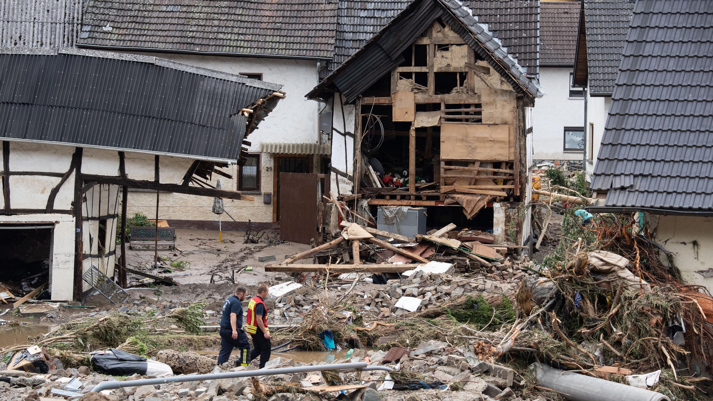 Rheinland-Pfalz, Schuld: Zwei Feuerwehrleute gehen in dem Dorf im Kreis Ahrweiler nach dem Unwetter mit Hochwasser durch den Schutt. Mindestens sechs Häuser wurden durch die Fluten zerstört.