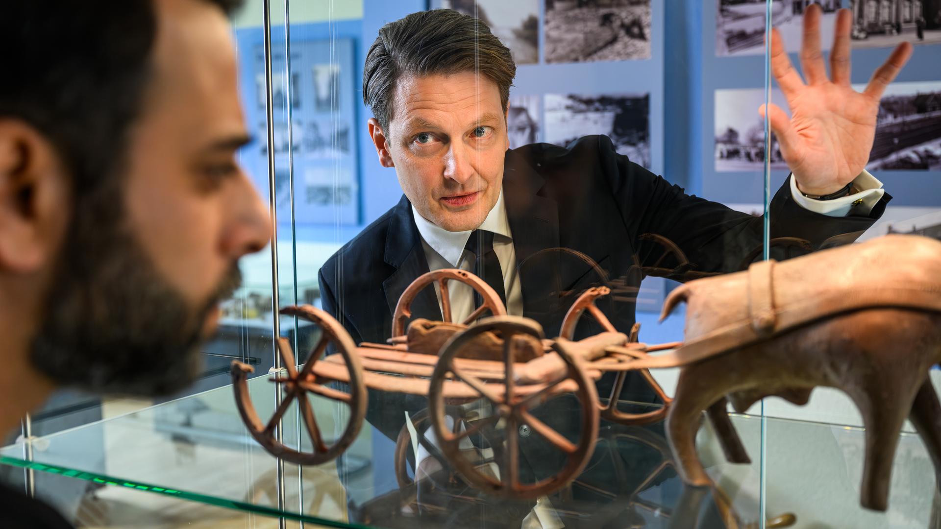 Yunus Özlügül (Yunus Cumartpay) und Wolfgang Habedank (Holger Stockhaus) betrachten konzentriert ein Ausstellungsstück in einer Vitrine, das wie ein antiker Wagen mit Rädern und einer Tierfigur aussieht